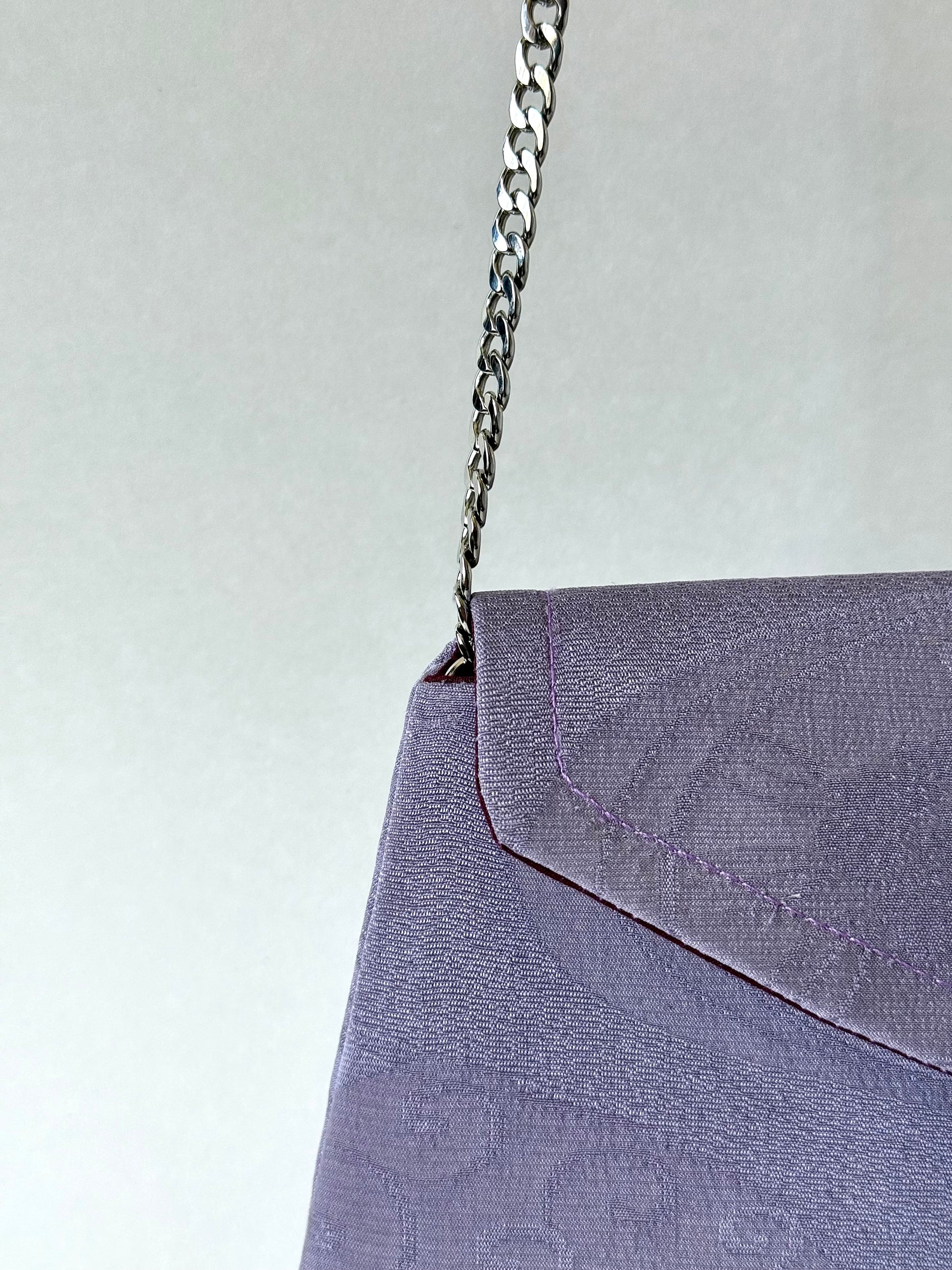 Close up view of silver colored metal chain coming out of the corner of the top interior side of a purple kimono silk clutch bag