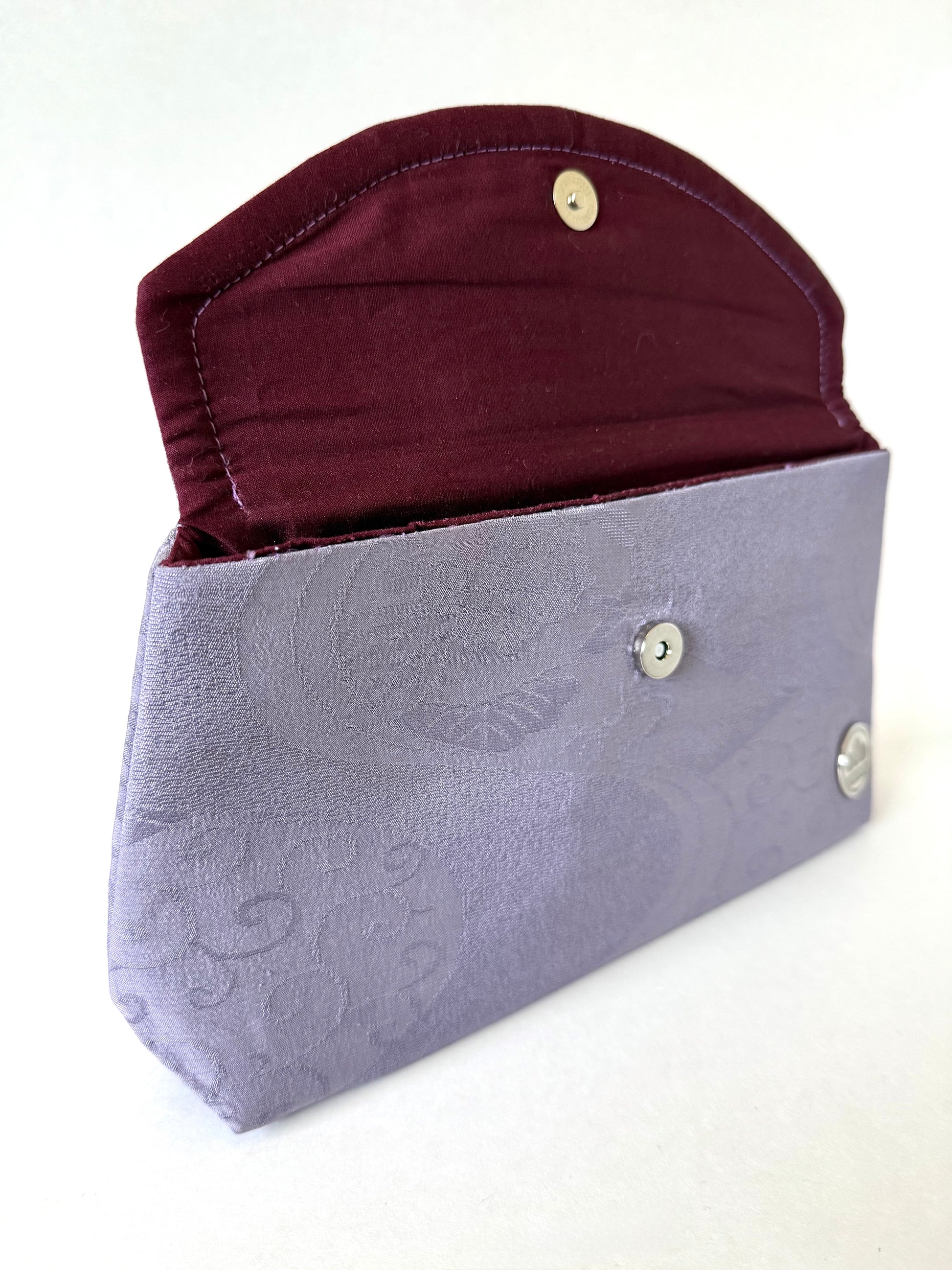 Opened flap on purple kimono silk fold-over clutch bag showing hand sewn seam and wine colored broadcloth interior lining