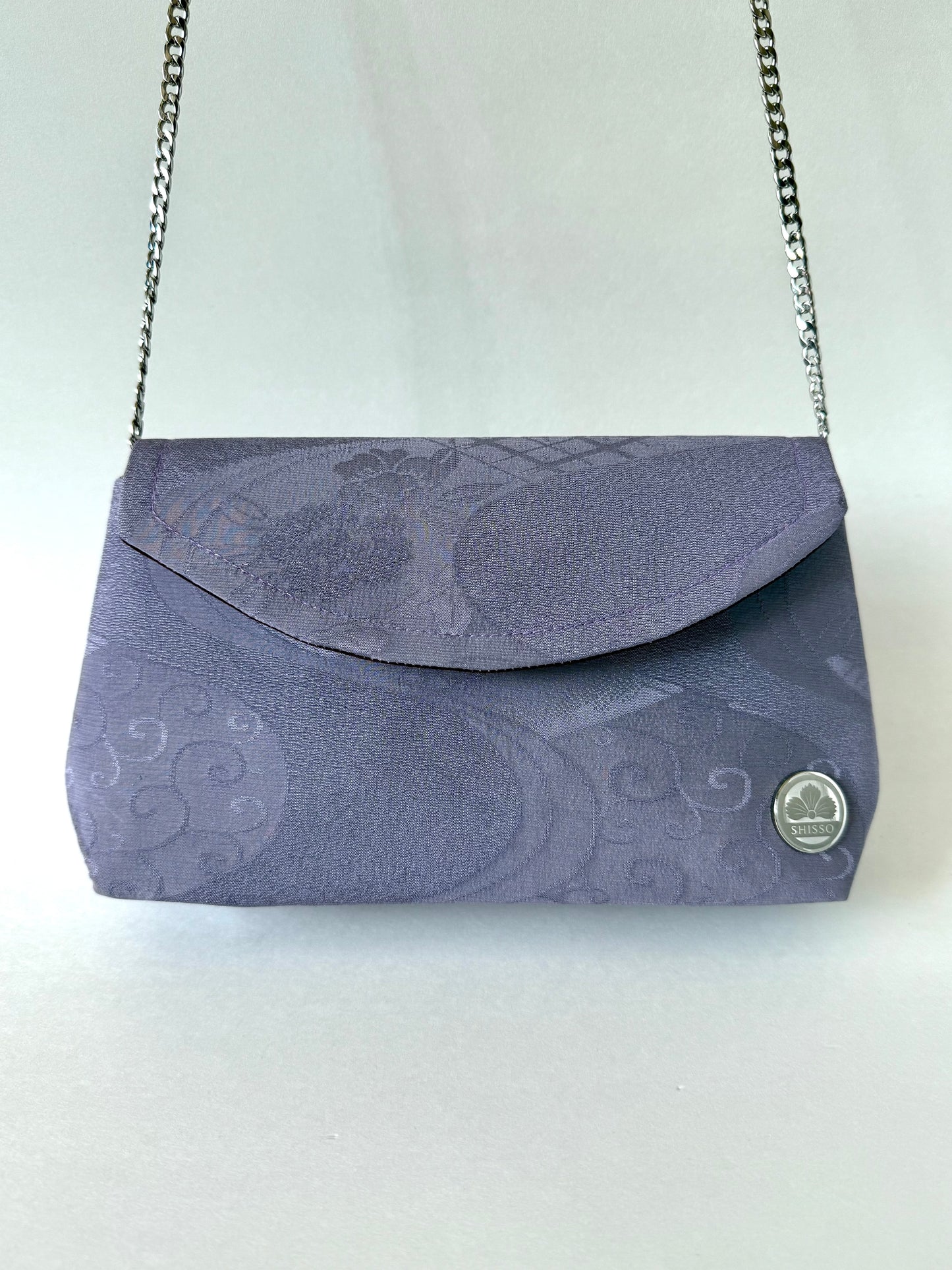 Front view of purple kimono silk clutch with floral and flowing water motifs hanging from silver colored metal chain strap 