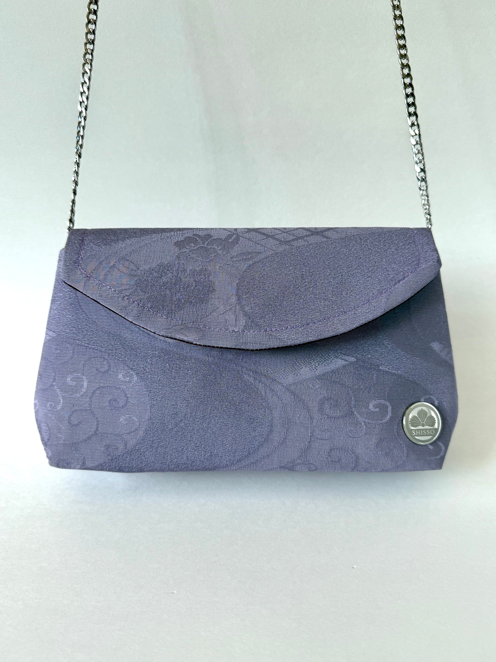 Front view of purple kimono silk clutch with floral and flowing water motifs hanging from silver colored metal chain strap 