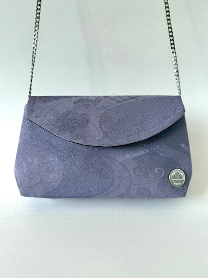 Front view of purple kimono silk clutch with floral and flowing water motifs hanging from silver colored metal chain strap 