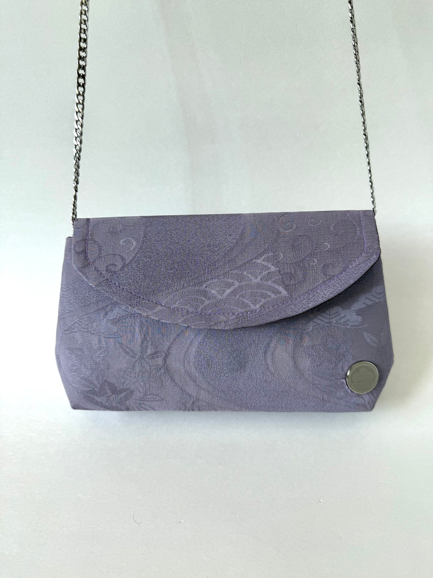 Front view of purple kimono silk clutch bag hanging from elegant metal chain strap