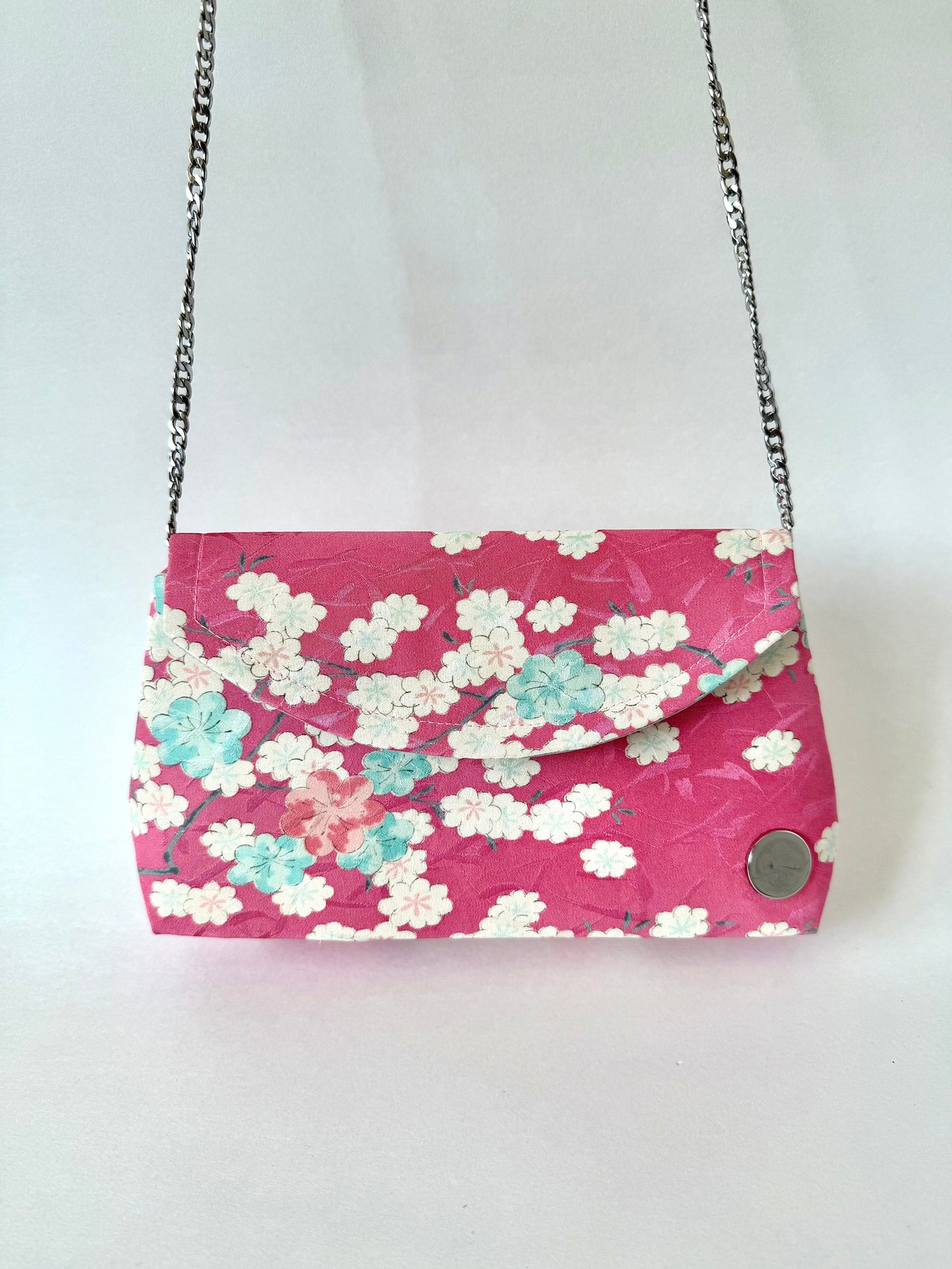 Pink kimono silk fold over clutch bag hanging from silver colored detachable metal chain strap