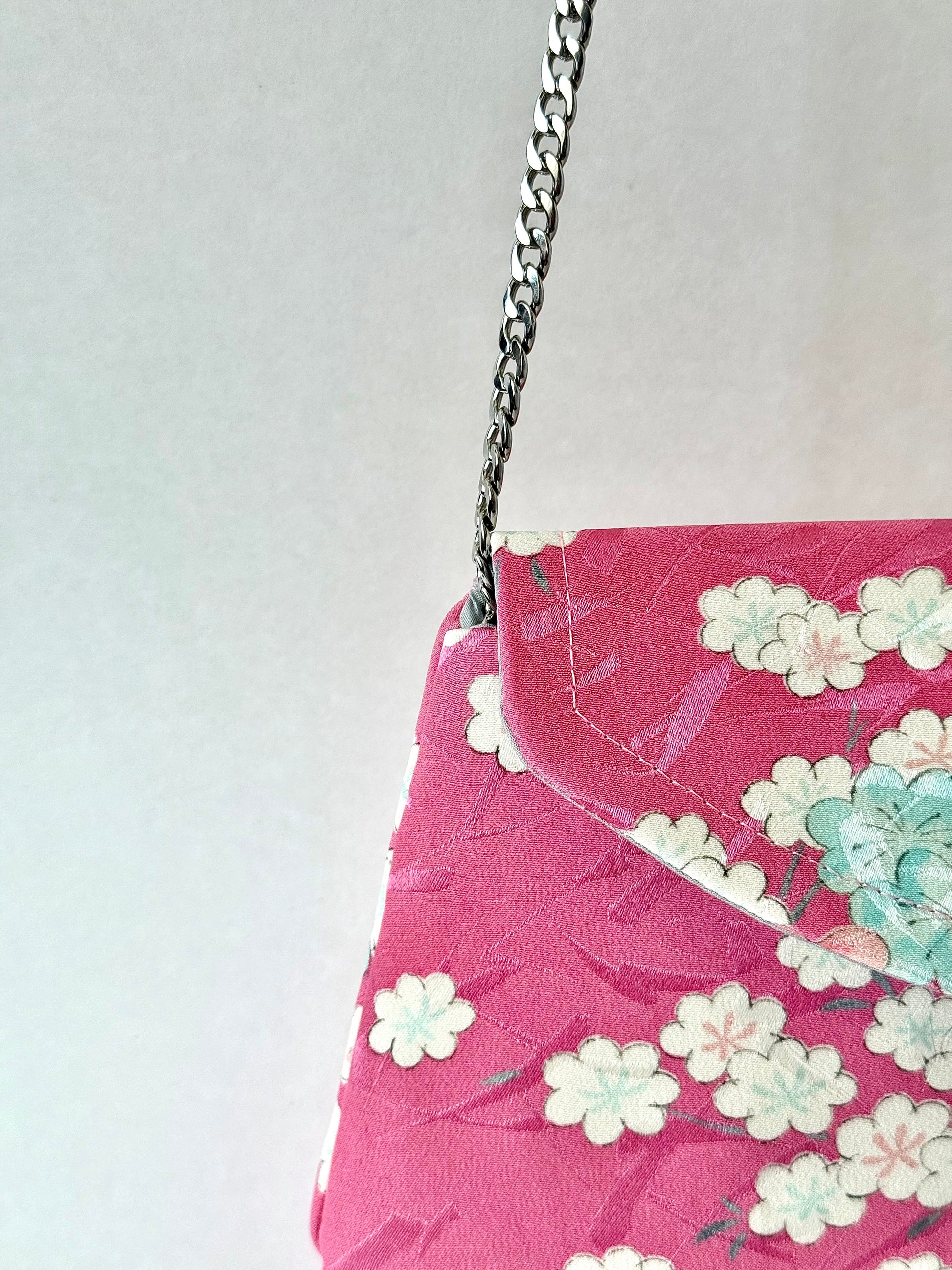 Close up of detachable metal chain link strap connected to fold over clutch with multi-colored cherry blossom motif