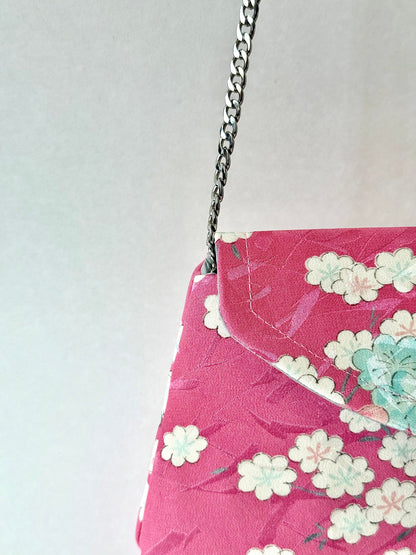 Close up of detachable metal chain link strap connected to fold over clutch with multi-colored cherry blossom motif