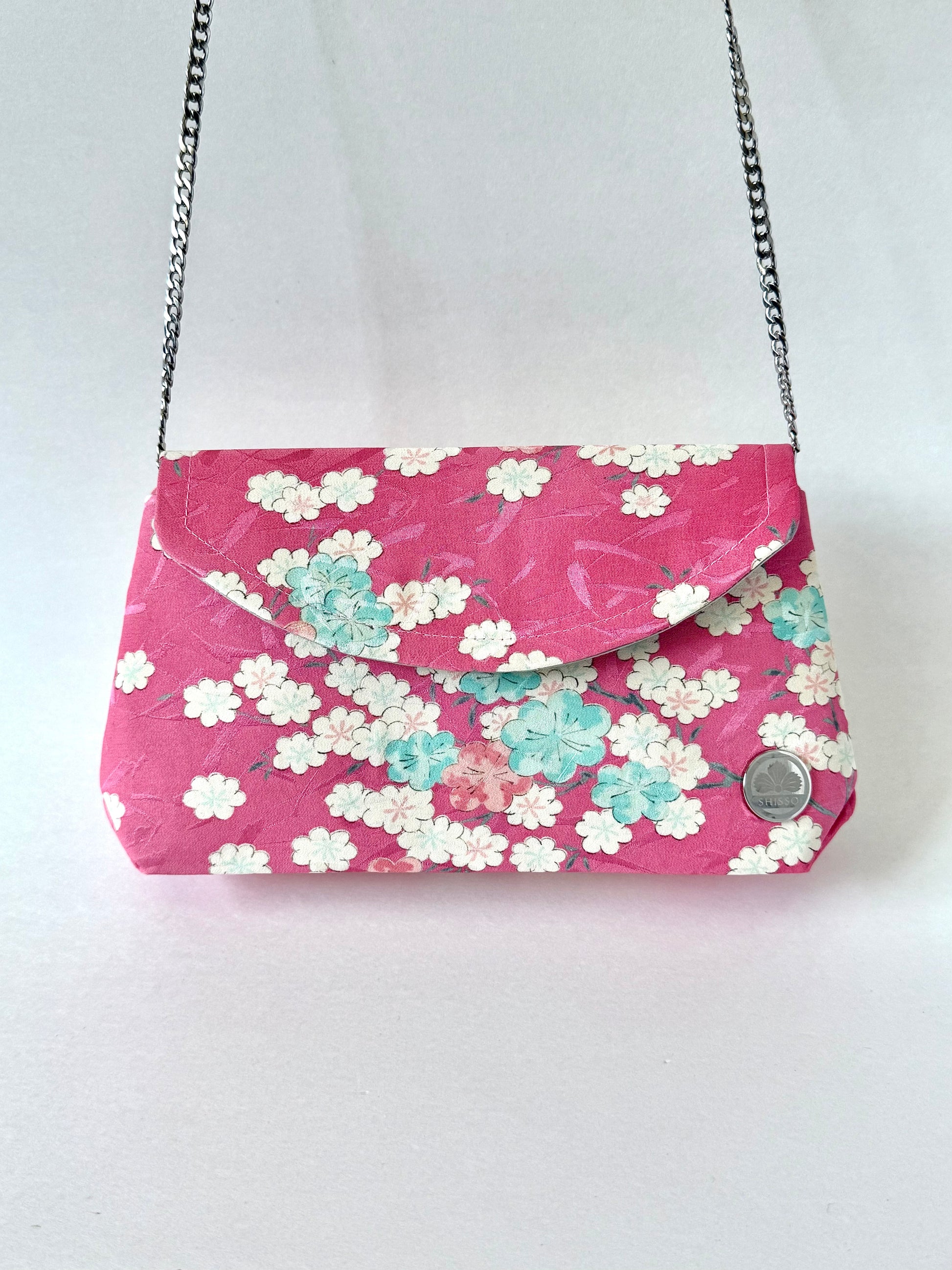 Pink kimono silk fold-over clutch bag hanging from detachable silver colored chain link strap