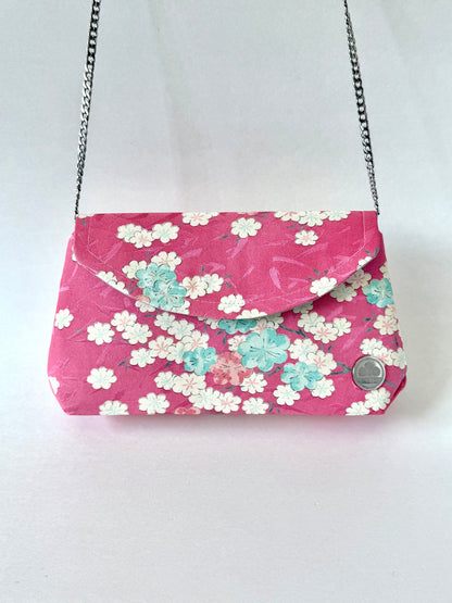 Pink kimono silk fold-over clutch bag hanging from detachable silver colored chain link strap