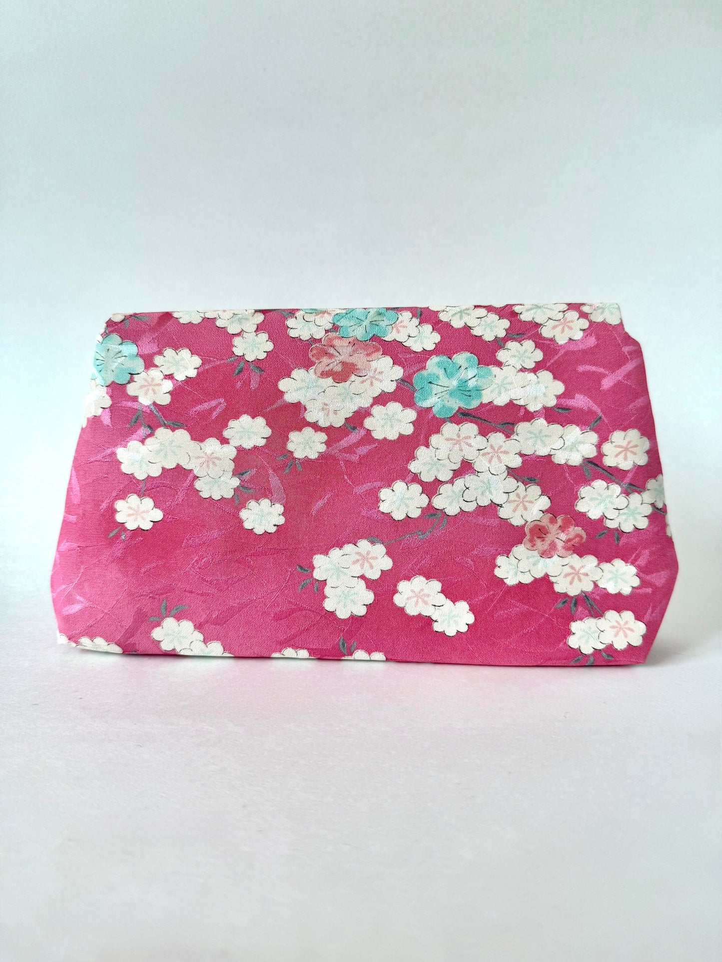 Backside view of pink kimono silk clutch bag showing mostly white cherry blossoms with a few pink and blue blossoms as well