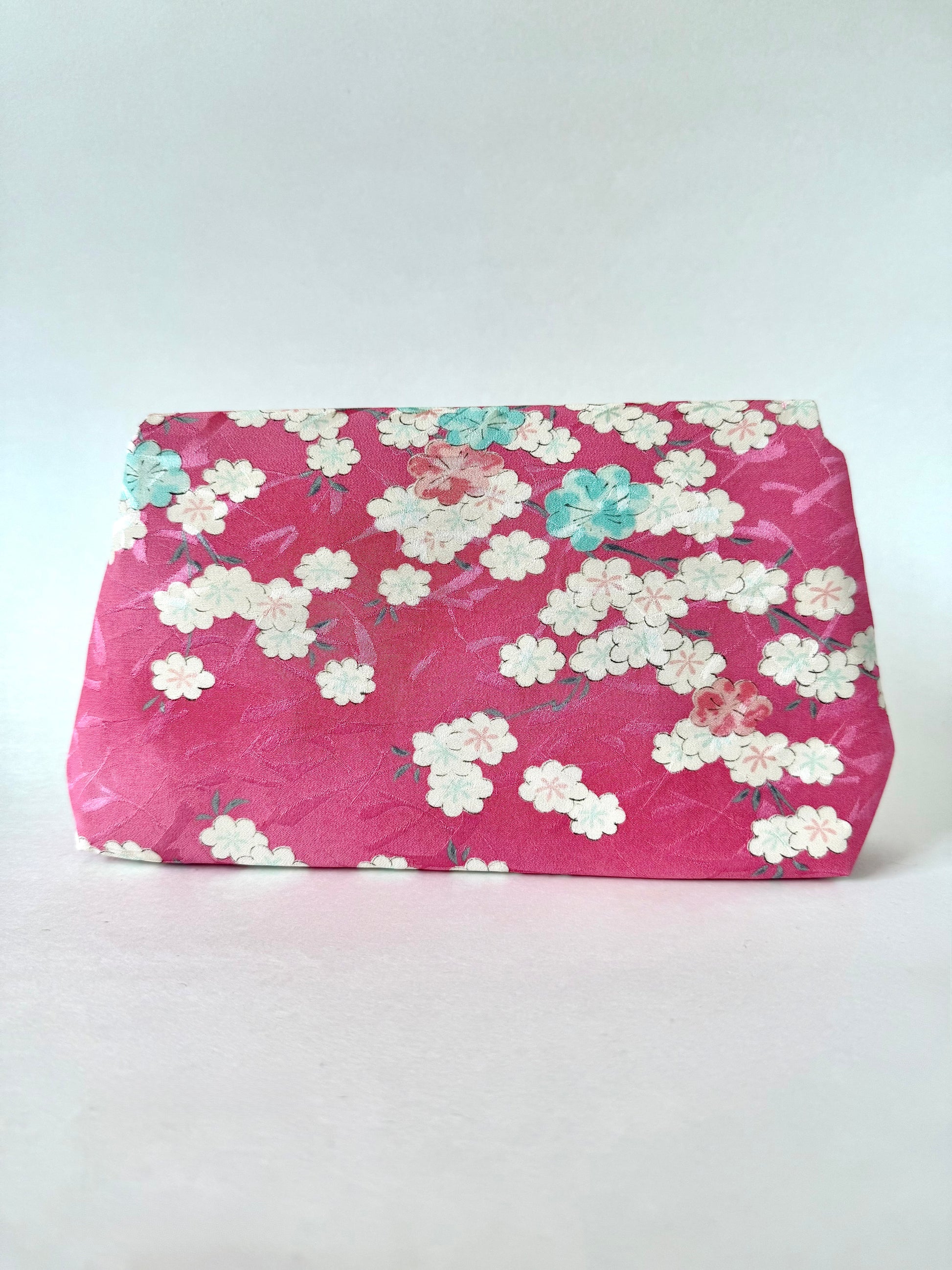 Backside view of pink kimono silk clutch bag showing mostly white cherry blossoms with a few pink and blue blossoms as well