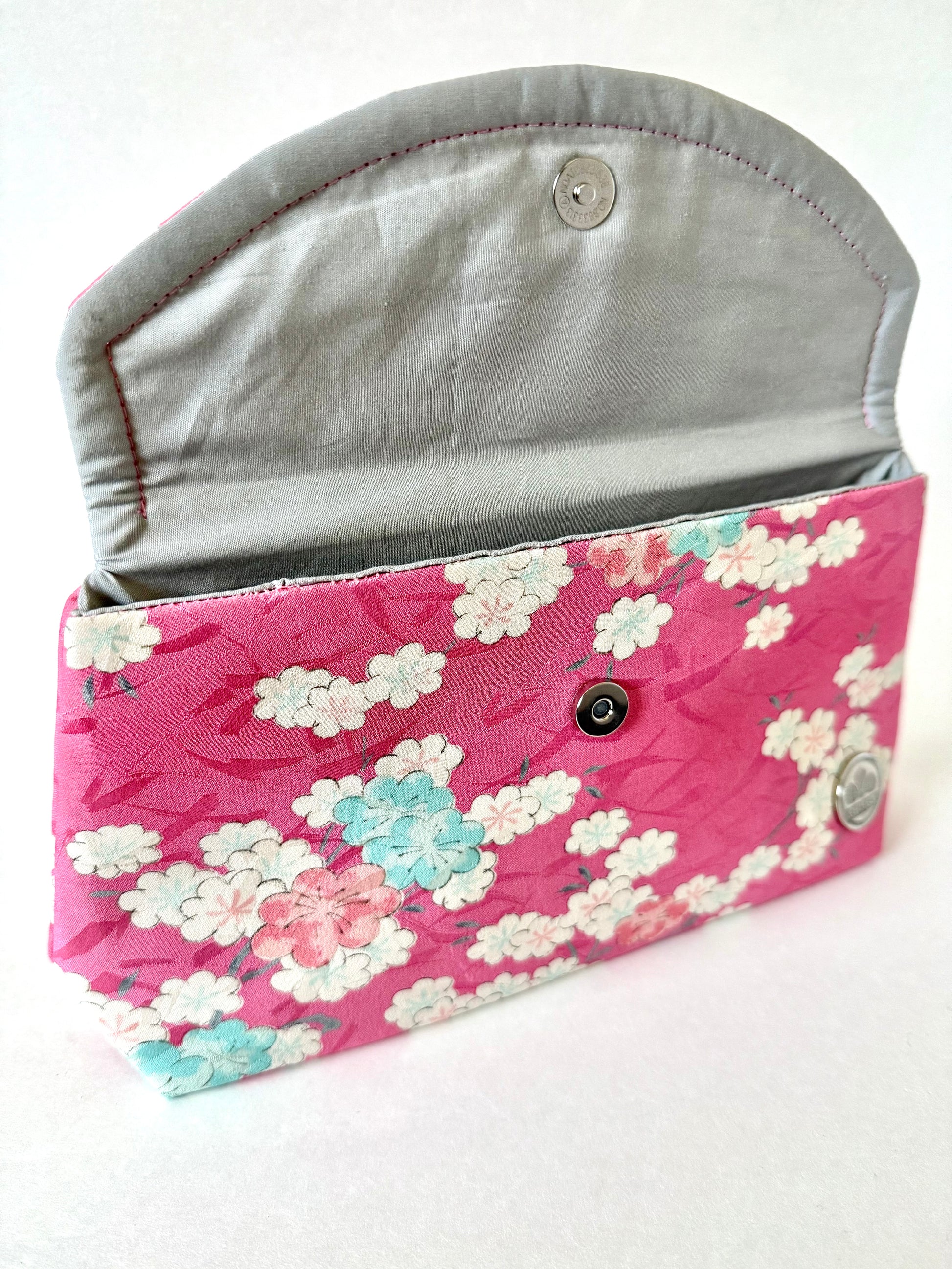 Hand stitched seam on pink kimono silk clutch bag with blue, white, and pink cherry blossoms and silver cotton interior
