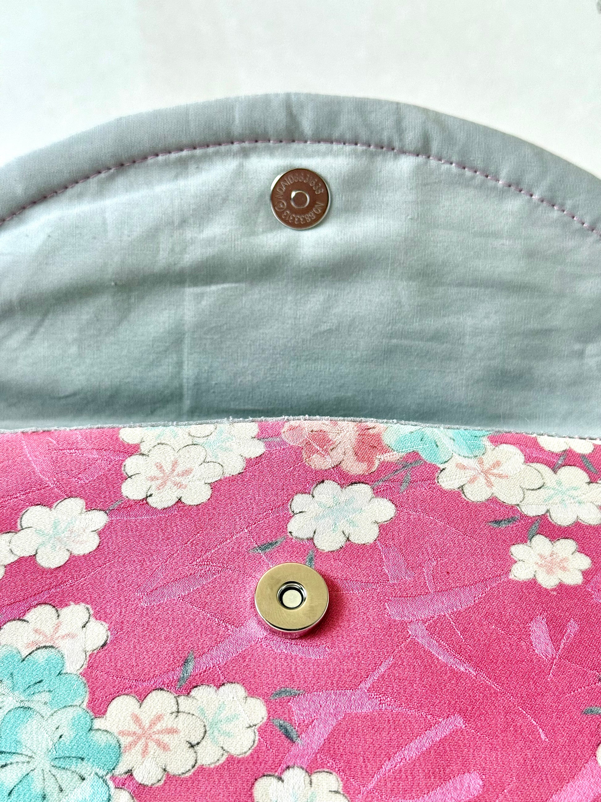 Silver colored magnetic closure on pink kimono silk clutch bag with sakura motif and shiny brush stroke like accents