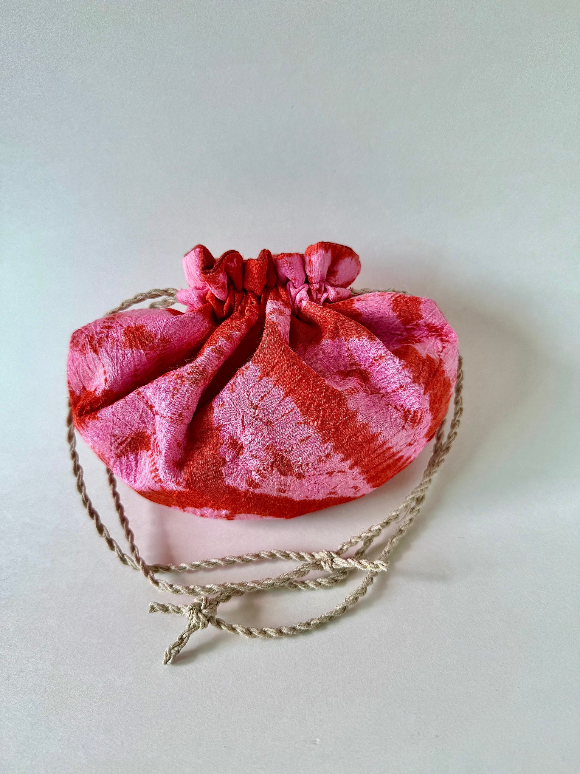 Back view of cinched red and pink shibori silk drawstring bag with natural hemp drawstrings
