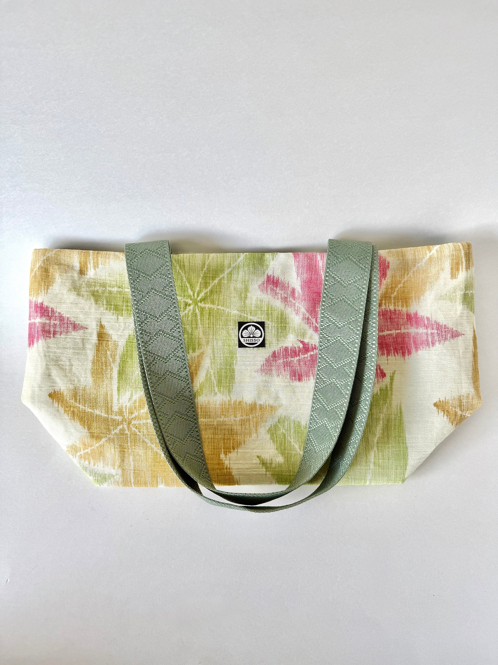 Front view of kimono silk tote bag laying flat with green, yellow, and red maple leaf motif